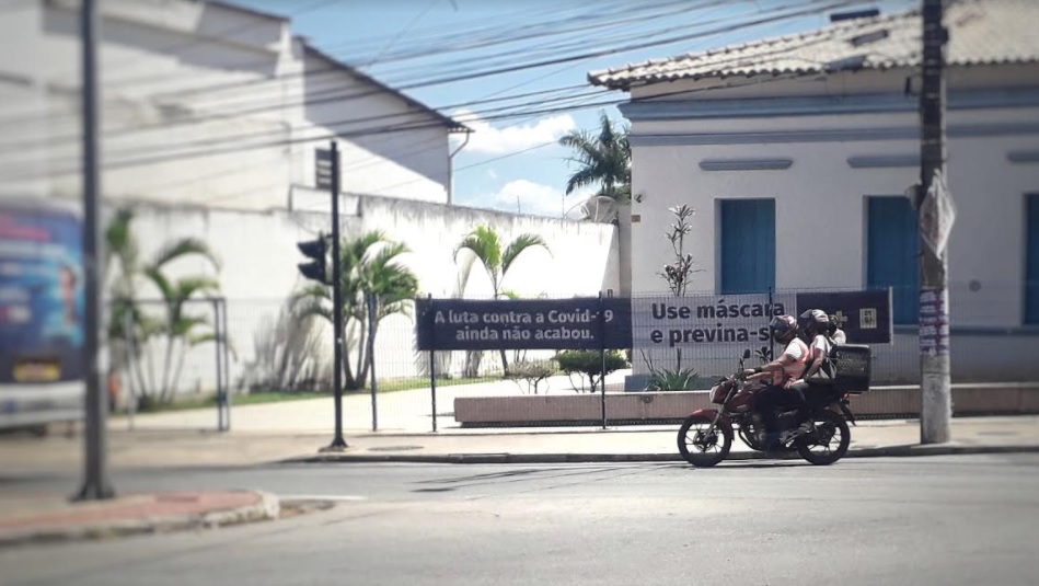 Motociclista em avenida do centro de Betim. Ao fundo, placa com orientações sobre a pandemia (Imagem Agenda Betim)