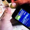 Dinheiro sendo contado, ao lado, um celular com o aplicativo Auxílio Emergencial do Governo Federal